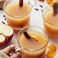 Mugs of hot spiced apple cider with a hand holding one mug