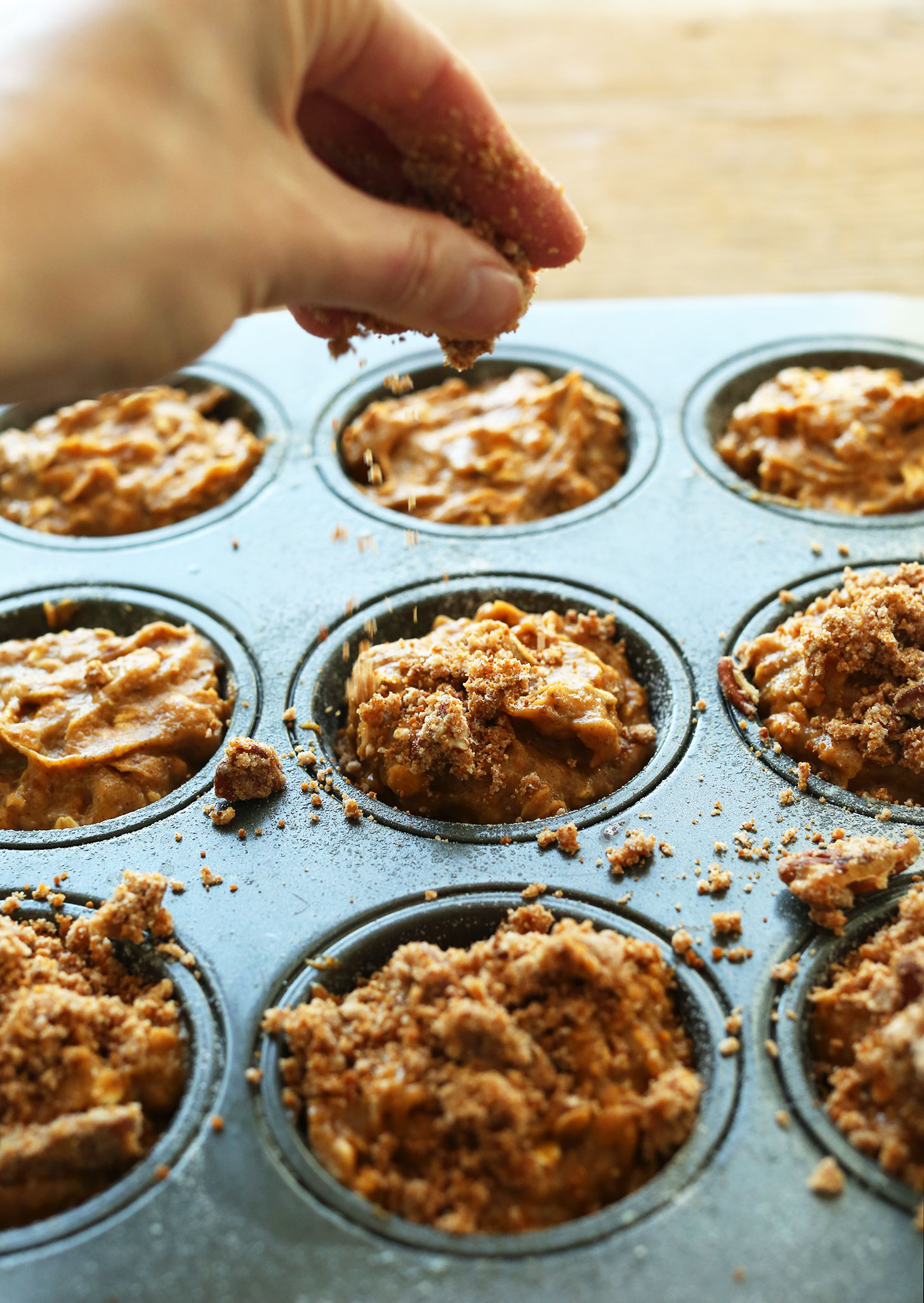 Sprinkling delicious Pecan Crumble Topping over gluten-free vegan Pumpkin Spices Muffins